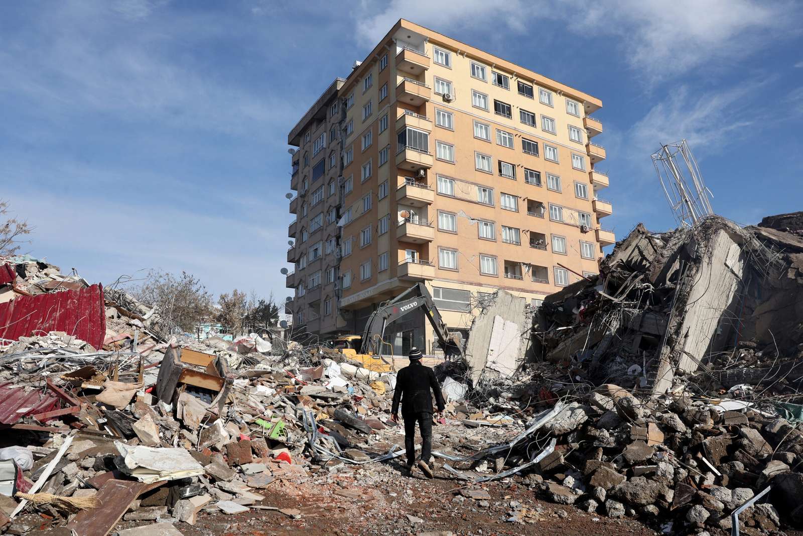 A man walks across the rubble of collapsed building towards a building still standing s in Kahramanmaras, close to the quake's epicentre, the day after a 7.8-magnitude earthquake struck the country's southeast, on February 7, 2023. - Rescuers in Turkey and Syria braved frigid weather, aftershocks and collapsing buildings, as they dug for survivors buried by an earthquake that killed more than 5,000 people. Some of the heaviest devastation occurred near the quake's epicentre between Kahramanmaras and Gaziantep, a city of two million where entire blocks now lie in ruins under gathering snow. (Photo by Adem ALTAN / AFP)