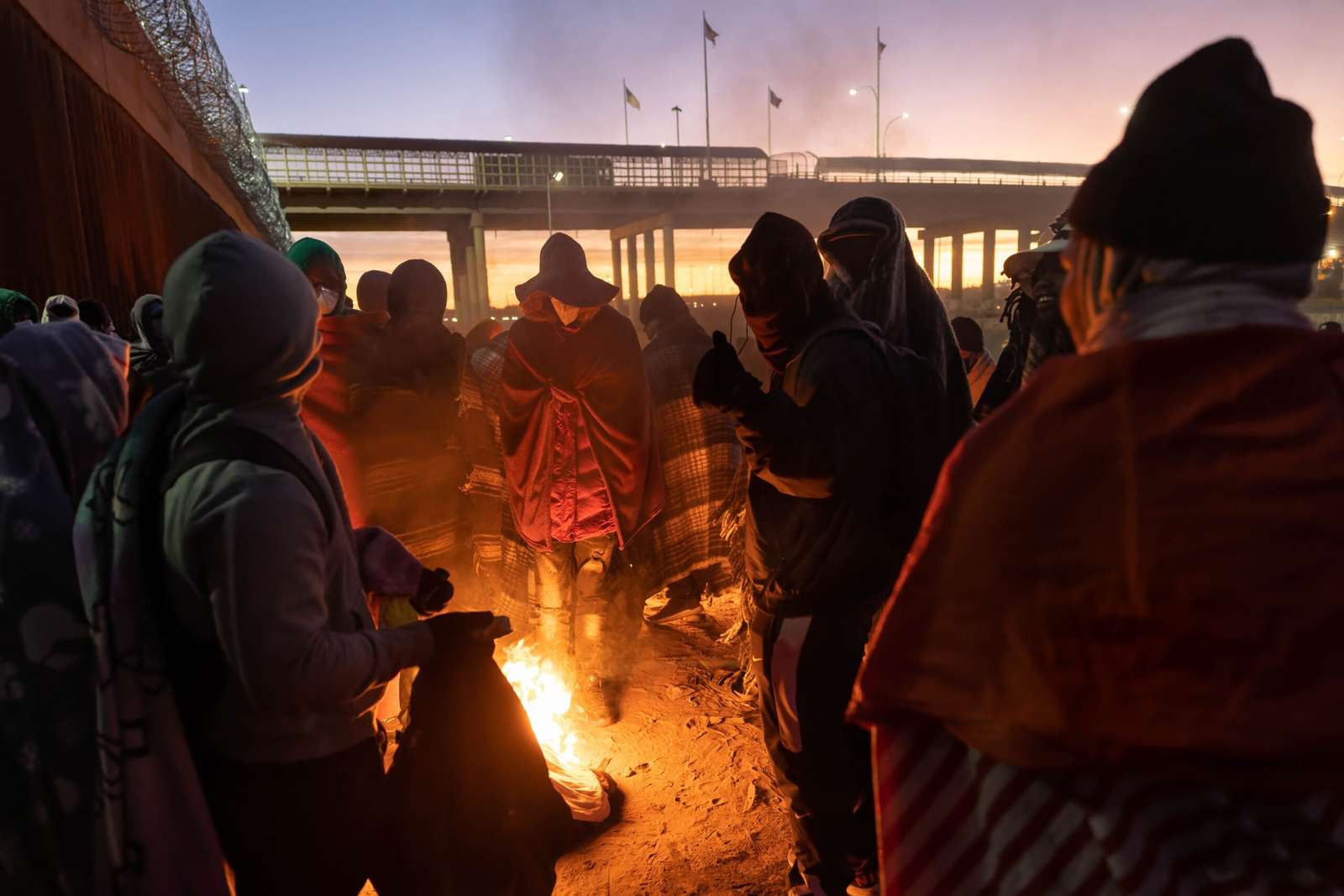 EL PASO, TEXAS - DECEMBER 22: Immigrants warm by a fire at dawn after spending a night alongside the U.S.-Mexico border fence on December 22, 2022 in El Paso, Texas. A spike in the number of migrants crossing over to seek asylum in the United States has challenged local, state and federal authorities. The numbers are expected to increase as the fate of the Title 42 authority to expel migrants remains in limbo pending a Supreme Court decision expected after Christmas.   John Moore/Getty Images/AFP (Photo by JOHN MOORE / GETTY IMAGES NORTH AMERICA / Getty Images via AFP)