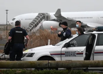 Funcionarios de aduanas de Francia vigilan el  Airbus A340 de Legend Airlines en el aeropuerto de Vatry, al este de París, donde los pasajeros indios fueron retenidos./AFP