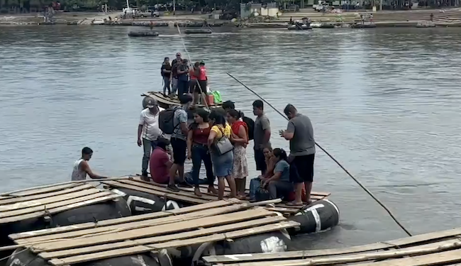 Un grupo de personas migrantes cruzan el río Suchiate entre Guatemala y México, en una balsa.